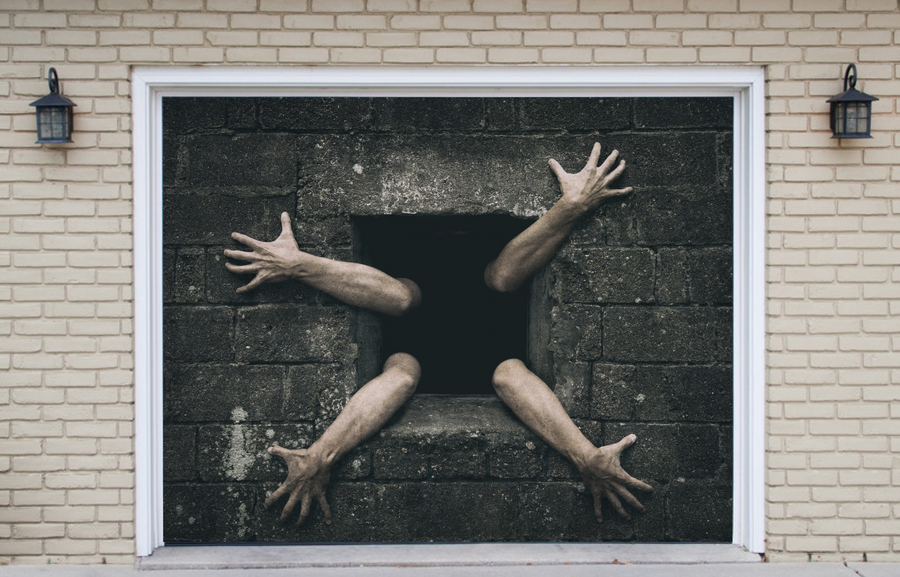 Manos asomando por una pequeña ventana en una pared de hormigón: decoración para la puerta del garaje.
